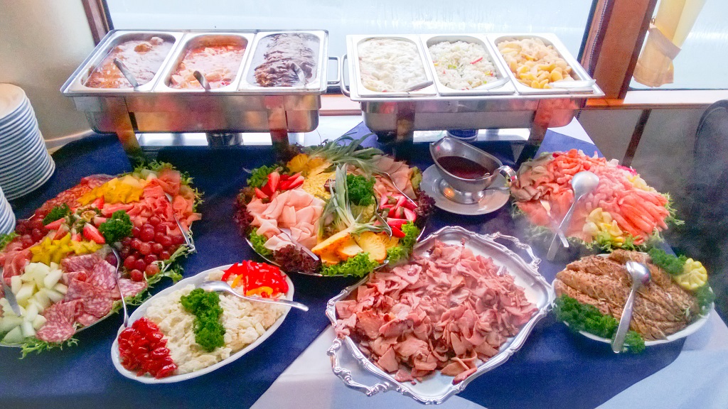 Uitgebreid buffet aan boord met warme gerechten in chafing dishes en diverse schalen met vleeswaren, salades, groenten en fruit.